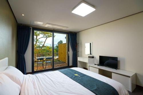 um quarto com uma cama, uma televisão e uma janela em Misoga Pension em Seogwipo