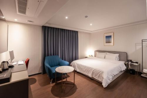 um quarto de hotel com uma cama e uma cadeira azul em Brown Dot Hotel Hadan em Busan