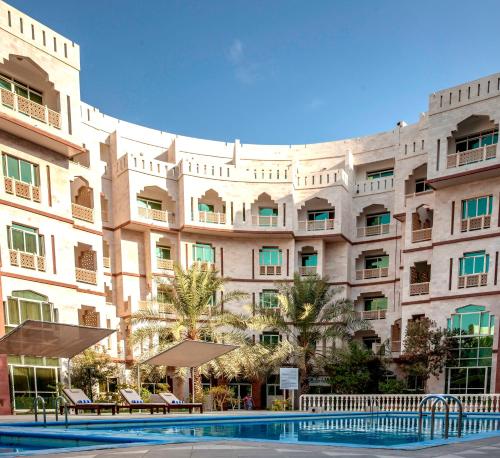 a large building with a swimming pool in front of it at Muscat Oasis Residences in Muscat