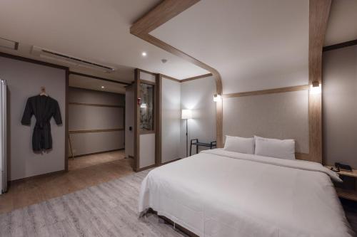 a bedroom with a large white bed and a robe at BELMORE Hotel in Busan