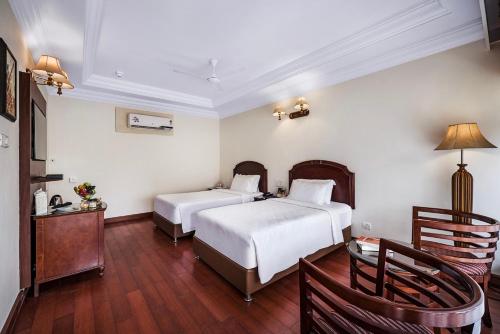a bedroom with two beds and a table and chairs at GReaT Trails Riverview Thanjavur By GRT Hotels in Thanjāvūr