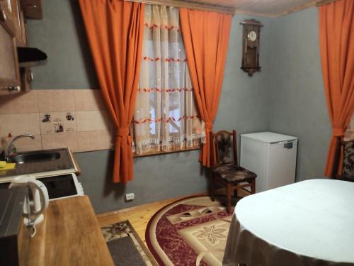 eine Küche mit orangefarbenen Vorhängen, einem Waschbecken und einem Tisch in der Unterkunft Садиба "Три Царі" in Jaremtsche