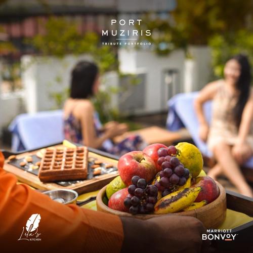 a person holding a tray of fruit on a table at Port Muziris, A Tribute Portfolio Hotel by Marriott in Nedumbassery
