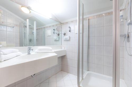 a white bathroom with a sink and a shower at Landhotel Häuserl im Wald in Gröbming