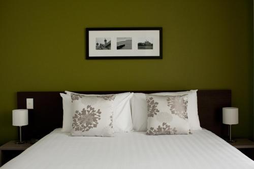 a bed with white pillows and a green wall at Quest Rotorua Central in Rotorua