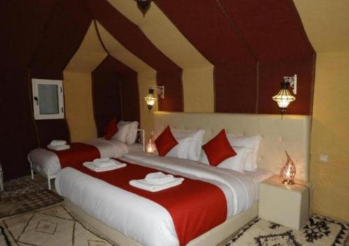 two beds in a hotel room with red sheets at Fantastic Desert Luxury Camp in Merzouga