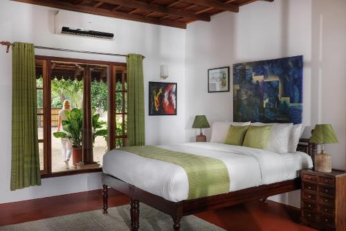 BluSalzz Escapade - Muhamma, Alleppey - Kerala في أليبي: غرفة نوم بسرير ونافذة فيها امرأة بالخارج
