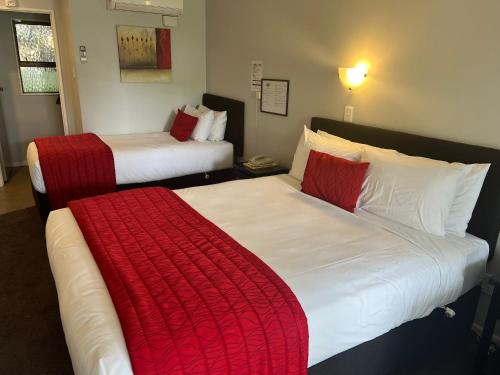 two beds in a hotel room with red and white blankets at Avenue Motel Palmerston North in Palmerston North