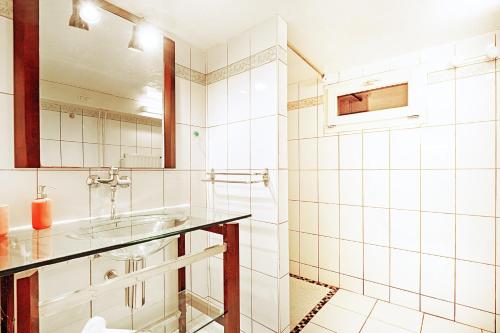 a white tiled bathroom with a sink and a mirror at Le Chalet Sous les Sapins - Superbe vue in Rochesson