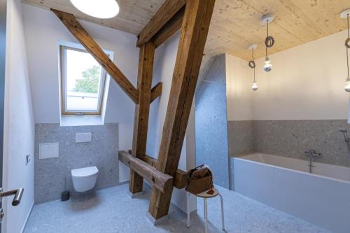 La salle de bains est pourvue d'un plafond en bois, d'une baignoire et de toilettes. dans l'établissement Landurlaub mit neugierigen Blicken in den Pferdestall, eingezäuntem Garten, Kamin und Sauna, à Rot am See