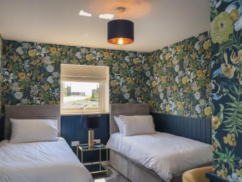 two beds in a room with floral wallpaper at Eala Bhàn Cottage in Carinish