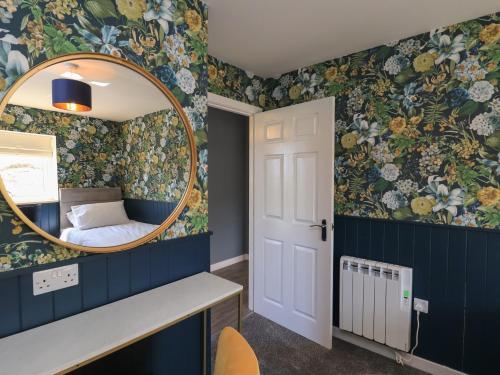 a bedroom with a mirror and floral wallpaper at Eala Bhàn Cottage in Carinish
