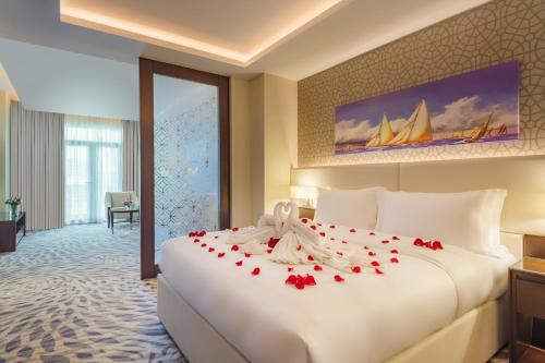 a hotel room with a large white bed with roses on it at Riviera Rayhaan by Rotana Doha in Doha