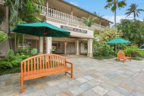 two benches and umbrellas in front of a hotel at Aston Islander On The Beach in Kapaa