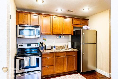 a kitchen with wooden cabinets and a stainless steel refrigerator at Breakfast Club - U of Tampa Flat in N Hyde Park in Tampa