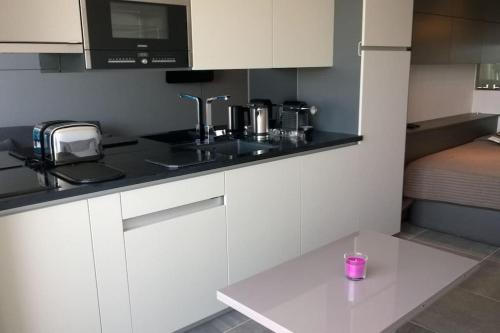 une cuisine avec des placards blancs et une bougie rose sur un comptoir dans l'établissement Studio 216, Héliopolis AB au village naturiste, au Cap d'Agde