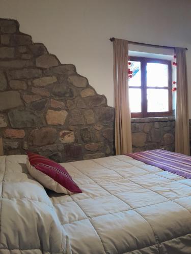Cama en habitación con pared de piedra en La Casa del Indio en Tilcara