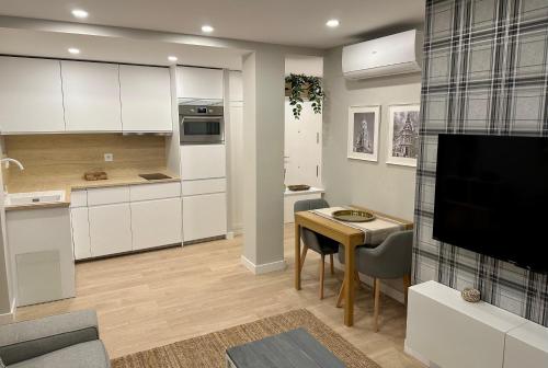 uma cozinha com armários brancos, uma mesa e uma televisão em Apartamentos Universidad em Múrcia