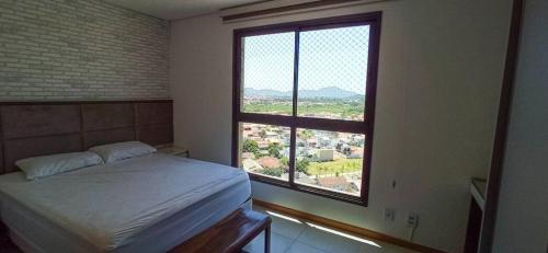 um quarto com uma cama e uma grande janela em Lindo Apto em Home Club na Praia Alegre em Penha