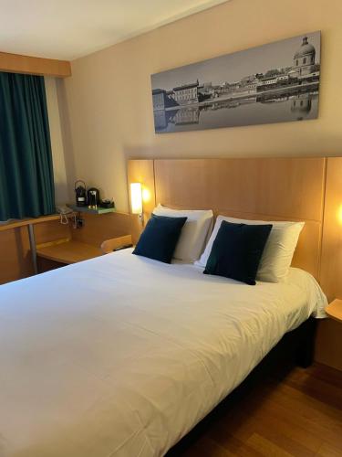 a bedroom with a large white bed with blue pillows at ibis Toulouse Aeroport in Blagnac