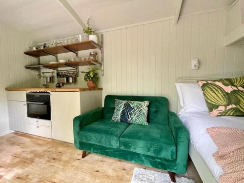 a green couch in a room with a kitchen at Cosy Shepherds Hut Lyme Regis in Uplyme
