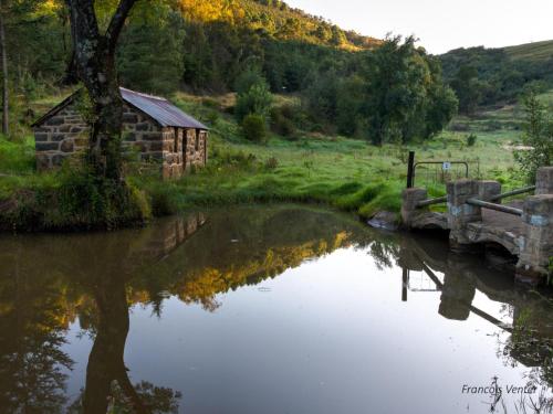 a barn next to a river with a reflection in the water at Flitwick Ranch in Swartberg