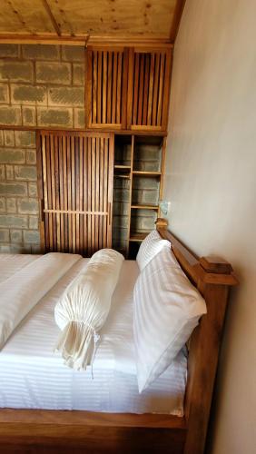 a bed with white pillows and a brick wall at Babylon Lodge in Marangu