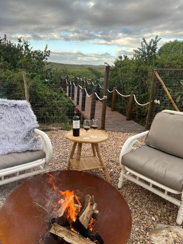 a fire pit with two chairs and a table with a bottle of wine at Ostrich cottage at Les Wings private game farm in Jongensfontein