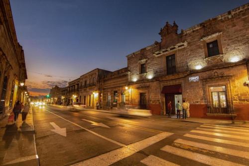 una calle de la ciudad por la noche con gente cruzando la calle en OYO Hostal Mich en Morelia