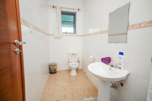 a white bathroom with a toilet and a sink at Beauty Hotel in Accra