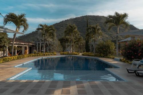 a swimming pool with palm trees and a mountain in the background at Hotel Campestre La María Toro Valle in Toro