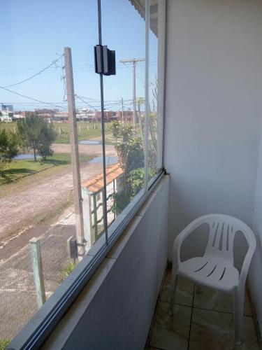 a white chair sitting on a balcony looking out a window at Apartamento família perto do mar in Tramandaí
