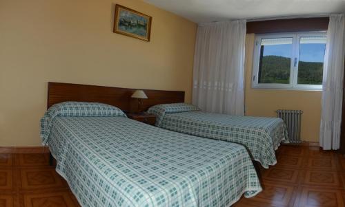 two beds in a hotel room with a window at Hostal Baviera in Pesués