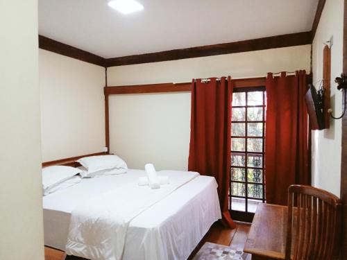 1 dormitorio con cama blanca y ventana en Pousada Le Lieu en Santo Antônio do Pinhal