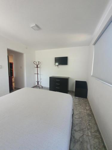 1 dormitorio con 1 cama blanca y TV en la pared en Casa om en San Roque