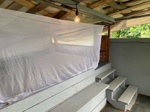Bett auf einer überdachten Veranda mit weißem Laken in der Unterkunft Camping para dos - a escoger segun disponibilidad de caseta o cabaña in Caguas