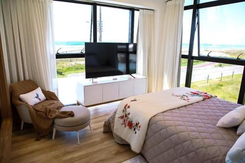 a bedroom with a television and a bed and a chair at Apto Pé na Areia com Piscina Privativa in Imbituba
