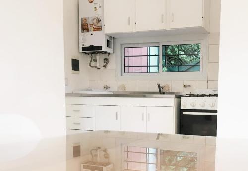 cocina blanca con armarios blancos y ventana en AMSTERDAM DEPARTAMENTOS en Villa Carlos Paz