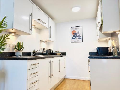 una cocina con armarios blancos y encimeras negras en City Centre Apartment Near the University and Bodleian Library, en Oxford