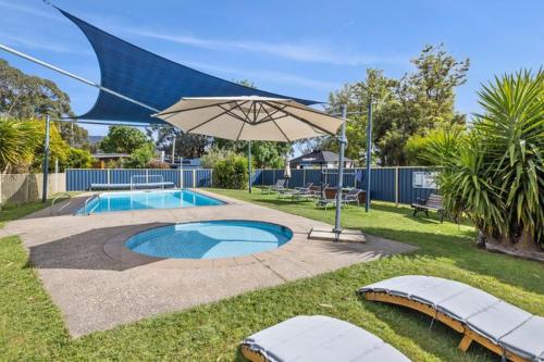 un patio con sombrilla y piscina en Halls Haven Holiday Units en Halls Gap