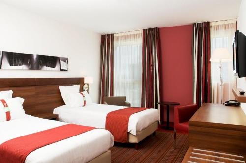 a hotel room with two beds and a desk at Holiday Inn Mulhouse by IHG in Mulhouse