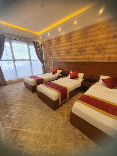 فندق فيفاء في فيفاء: ثلاثة أسرة في غرفة بجدران خشبية ونوافذ