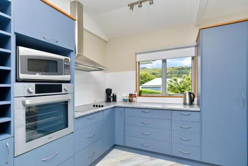 a kitchen with blue cabinets and a microwave at Watson Street - Bookahome in Akaroa