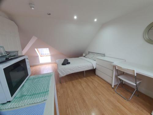 a small room with a bed and a desk and a television at Eastwood Rooms in Goodmayes