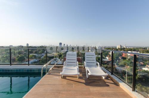 three white chairs sitting on the edge of a swimming pool at Comfortable Los Laureles Loft in Asuncion