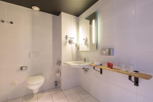 een badkamer met een toilet, een wastafel en een spiegel bij Leonardo Hotel Almere City Center in Almere