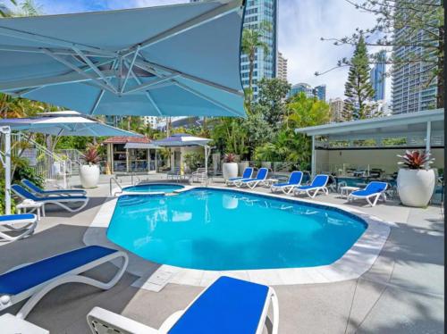 una piscina con sillas y sombrillas azules en Copacabana Apartments, en Gold Coast