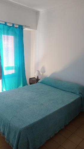 1 dormitorio con cama con colcha azul y ventana en El Dorado Deptos a una cuadra del mar en San Bernardo