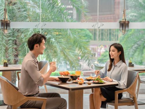 Ein Mann und eine Frau sitzen am Tisch und essen Essen. in der Unterkunft Sheraton Guangzhou Hotel in Guangzhou