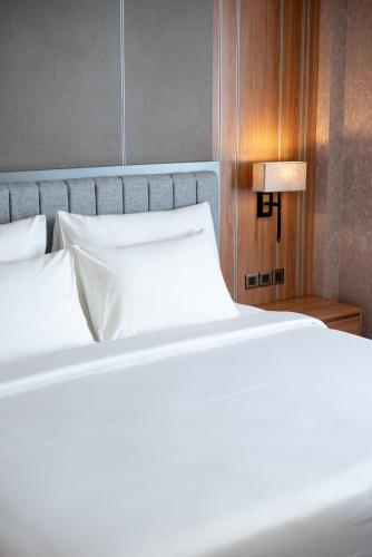 a bed with white sheets and a lamp on a table at Taman Prakerti Bhuana Hotel in Gianyar